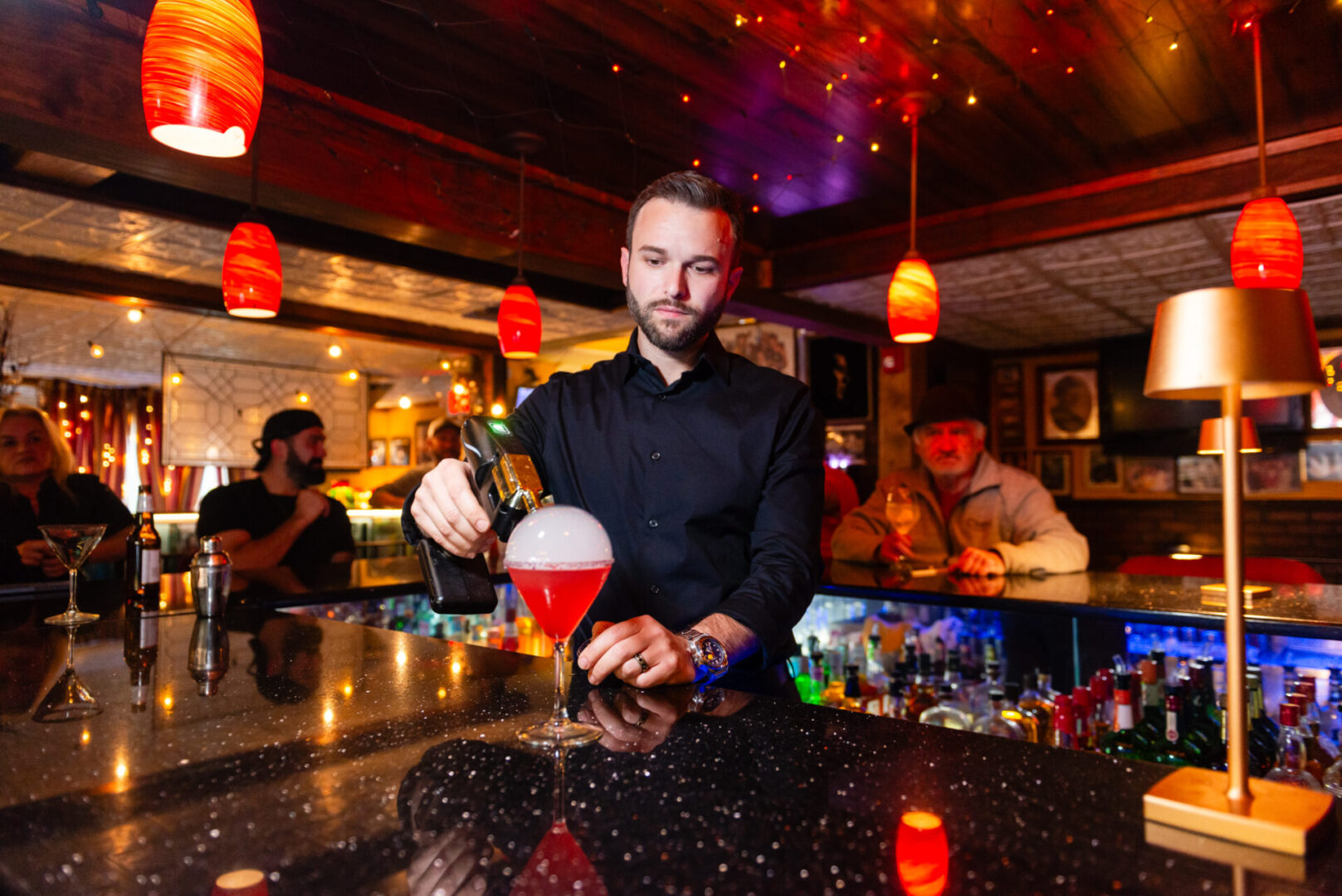 A man making a drink wearing black dress on the bar counter